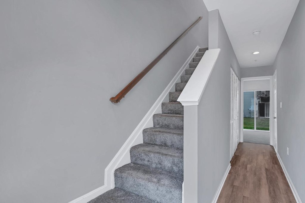 a gray carpeted staircase with a wooden handrail and a white wall